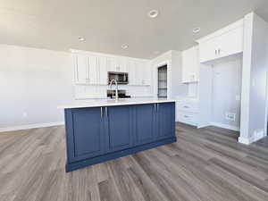 Kitchen featuring light hardwood / wood-style floors, white cabinetry, a kitchen island with sink, and tasteful backsplash