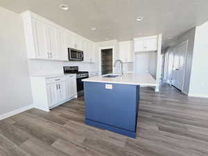 Kitchen with an island with sink, light wood-type flooring, sink, white cabinetry, and appliances with stainless steel finishes