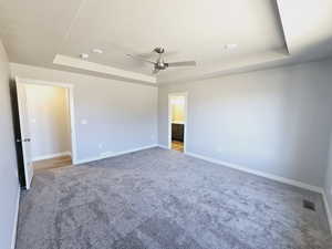 Unfurnished bedroom featuring ceiling fan, light carpet, a tray ceiling, and connected bathroom