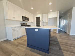 Kitchen with an island with sink, tasteful backsplash, light hardwood / wood-style flooring, white cabinetry, and stainless steel appliances