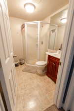 Bathroom with tile patterned flooring, toilet, a shower with door, vanity, and a textured ceiling