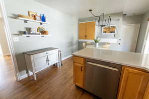 Kitchen with light stone countertops, stainless steel dishwasher, dark hardwood / wood-style floors, pendant lighting, and an inviting chandelier