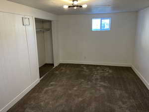 Unfurnished bedroom featuring dark carpet, a textured ceiling, and a closet