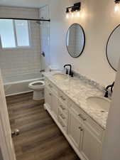 Full bathroom with hardwood / wood-style floors, vanity, tiled shower / bath combo, and toilet