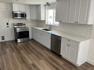 Kitchen with white cabinets, sink, backsplash, appliances with stainless steel finishes, and dark hardwood / wood-style flooring