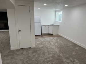 Interior space with carpet floors, a textured ceiling, white fridge, and white cabinetry