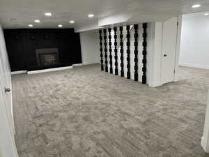 Basement with carpet flooring, a textured ceiling, and a wood stove