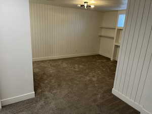 Unfurnished room with dark carpet, a textured ceiling, and wood walls