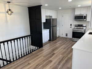 Kitchen featuring tasteful backsplash, hardwood / wood-style flooring, pendant lighting, white cabinetry, and appliances with stainless steel finishes