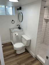 Bathroom featuring a tile shower, toilet, vanity, and wood-type flooring