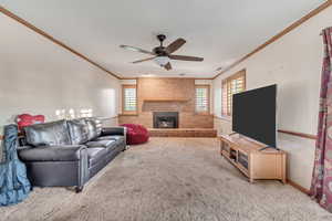 Living room featuring ceiling fan, ornamental molding, a fireplace, and carpet flooring