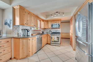 Kitchen with appliances with stainless steel finishes, light tile patterned flooring, tasteful backsplash, light brown cabinets, and sink