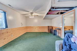 Unfurnished room featuring wooden walls, dark colored carpet, and ceiling fan