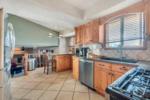 Kitchen with light tile patterned floors, sink, tasteful backsplash, decorative light fixtures, and appliances with stainless steel finishes