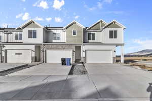 View of property featuring a garage, concrete driveway, stone siding, a mountain view, and board and batten siding