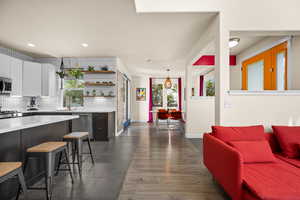 Kitchen with tasteful backsplash, a kitchen breakfast bar, dark wood-type flooring, white cabinets, and appliances with stainless steel finishes