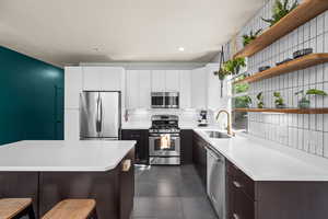 Kitchen featuring dark brown cabinetry, sink, white cabinetry, stainless steel appliances, and decorative backsplash