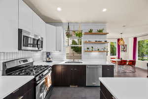 Kitchen with dark brown cabinets, sink, stainless steel appliances, hanging light fixtures, and white cabinetry