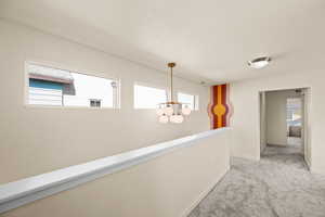 Corridor with light carpet, a wealth of natural light, and an inviting chandelier