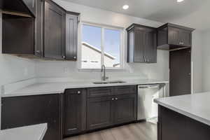 Kitchen with sink, light stone counters, dark brown cabinets, light hardwood / wood-style flooring, and stainless steel dishwasher