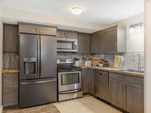 Kitchen with light hardwood / wood-style flooring, appliances with stainless steel finishes, tasteful backsplash, and sink