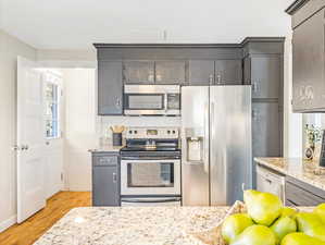 Kitchen featuring light hardwood / wood-style flooring, appliances with stainless steel finishes, gray cabinets, and light stone countertops