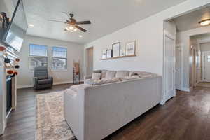 Living room with ceiling fan, a textured ceiling, and dark wood-type flooring