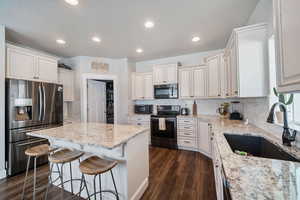 Kitchen with light stone counters, a center island, stainless steel appliances, sink, and dark hardwood / wood-style flooring