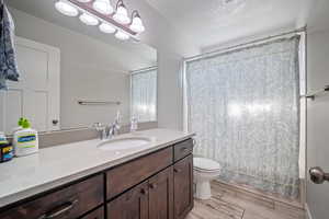 Bathroom with toilet, curtained shower, hardwood / wood-style flooring, vanity, and a textured ceiling