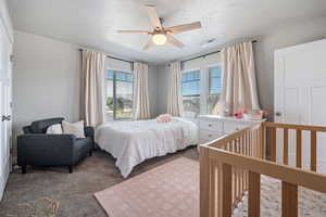 Carpeted bedroom featuring a textured ceiling, multiple windows, and ceiling fan