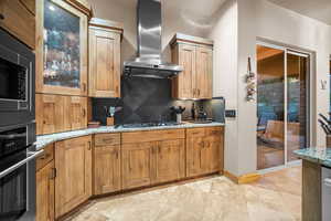 Kitchen with light stone countertops, stainless steel appliances, tasteful backsplash, and wall chimney range hood