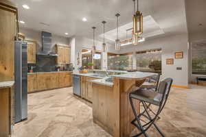 Kitchen with a raised ceiling, a large island, decorative light fixtures, wall chimney range hood, and a breakfast bar area