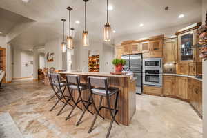 Kitchen featuring light stone countertops, stainless steel appliances, hanging light fixtures, a center island with sink, and a kitchen breakfast bar