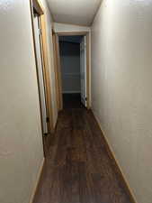 Hall with a textured ceiling and dark hardwood / wood-style floors