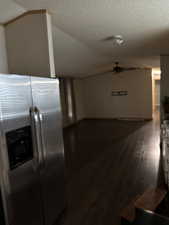 Kitchen featuring stainless steel fridge, dark wood-type flooring, white cabinetry, vaulted ceiling, and a textured ceiling