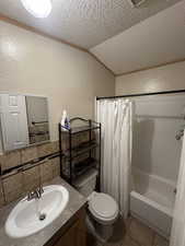 Full bathroom featuring tile patterned flooring, shower / bath combo, vaulted ceiling, toilet, and a textured ceiling