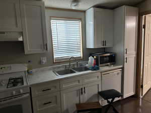 Kitchen with white cabinets, sink, white appliances, and range hood