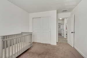 Bedroom with a closet, a crib, and light colored carpet