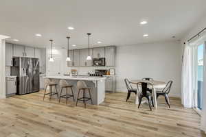 Kitchen with pendant lighting, gray cabinets, appliances with stainless steel finishes, and light wood-type flooring