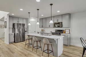 Kitchen featuring an island with sink, sink, stainless steel appliances, and light hardwood / wood-style flooring