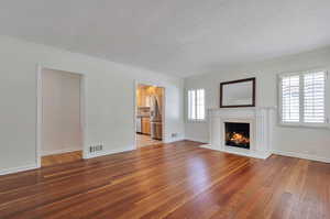 Unfurnished living room with a textured ceiling, a fireplace, ornamental molding, and hardwood / wood-style floors