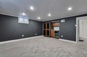 Basement with light carpet, wine cooler, wood walls, and ornamental molding