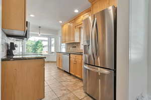 Kitchen featuring dark stone counters, light tile patterned flooring, stainless steel appliances, backsplash, and light brown cabinets