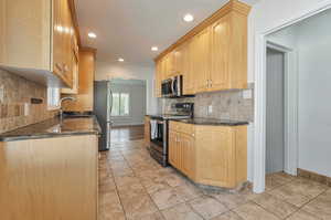 Kitchen with appliances with stainless steel finishes, dark stone counters, sink, and light brown cabinets