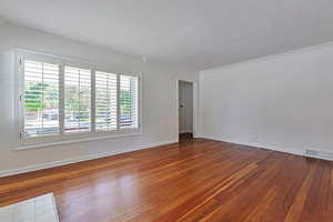 Empty room with a textured ceiling, a healthy amount of sunlight, crown molding, and hardwood / wood-style flooring