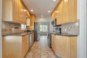 Kitchen featuring light brown cabinets, sink, tasteful backsplash, stainless steel appliances, and dark stone counters