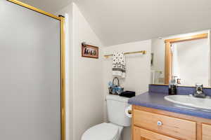 Bathroom with walk in shower, vanity, lofted ceiling, and toilet