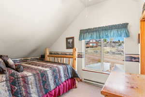 Bedroom with vaulted ceiling, a baseboard heating unit, and light carpet