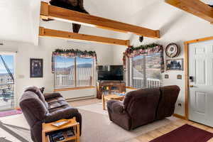 Carpeted living room with baseboard heating, beam ceiling, and high vaulted ceiling