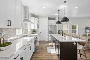 Kitchen featuring white cabinets, sink, a center island with sink, wall chimney range hood, and appliances with stainless steel finishes